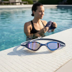 luwa Apex Elite navy blue swimming goggles with anti-fog coating and UV protection, on pool deck next to swim cap and fins.