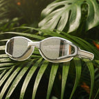 LUWA Apex Elite white and silver sport goggles with anti-fog coating and UV protection, resting on a palm leaf.