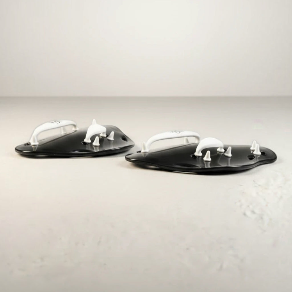 luwa Flow Paddles in black and white, designed for swimming training to build arm strength and refine technique. Features ergonomic shape and adjustable straps.