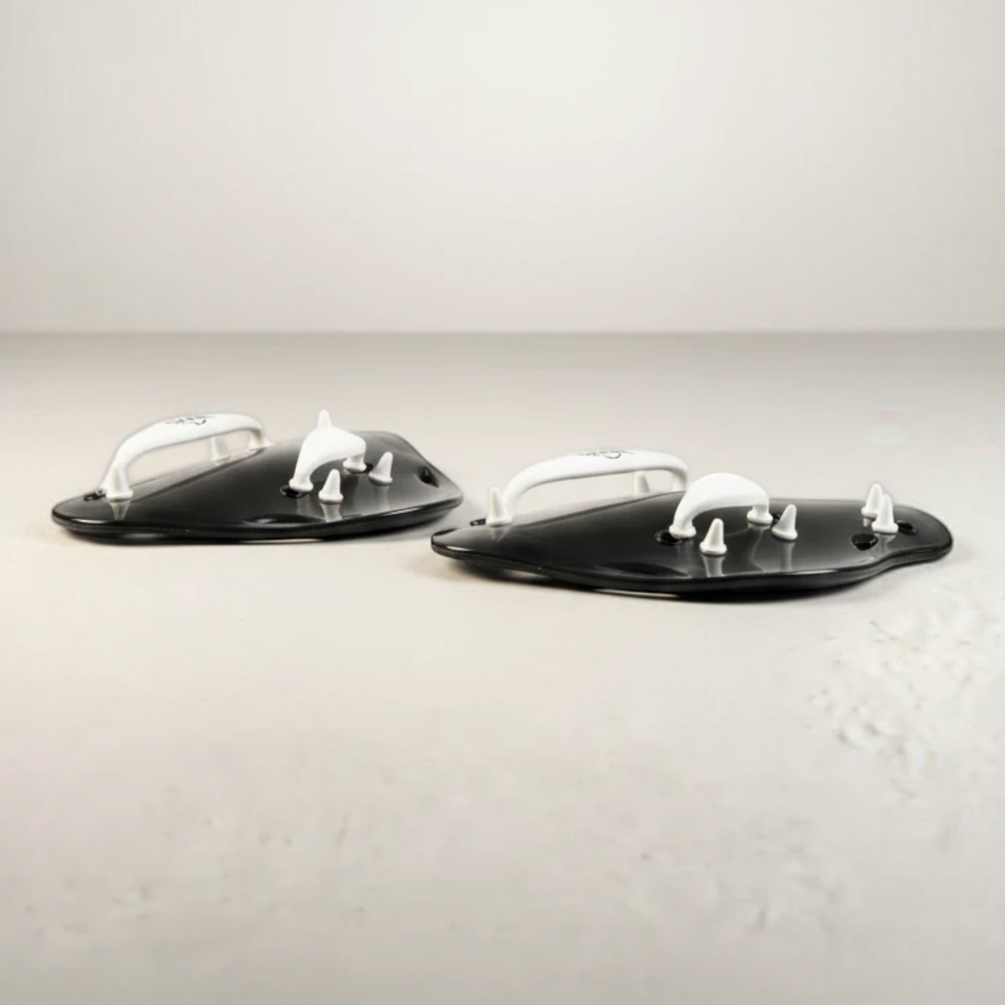 luwa Flow Paddles in black and white, designed for swimming training to build arm strength and refine technique. Features ergonomic shape and adjustable straps.